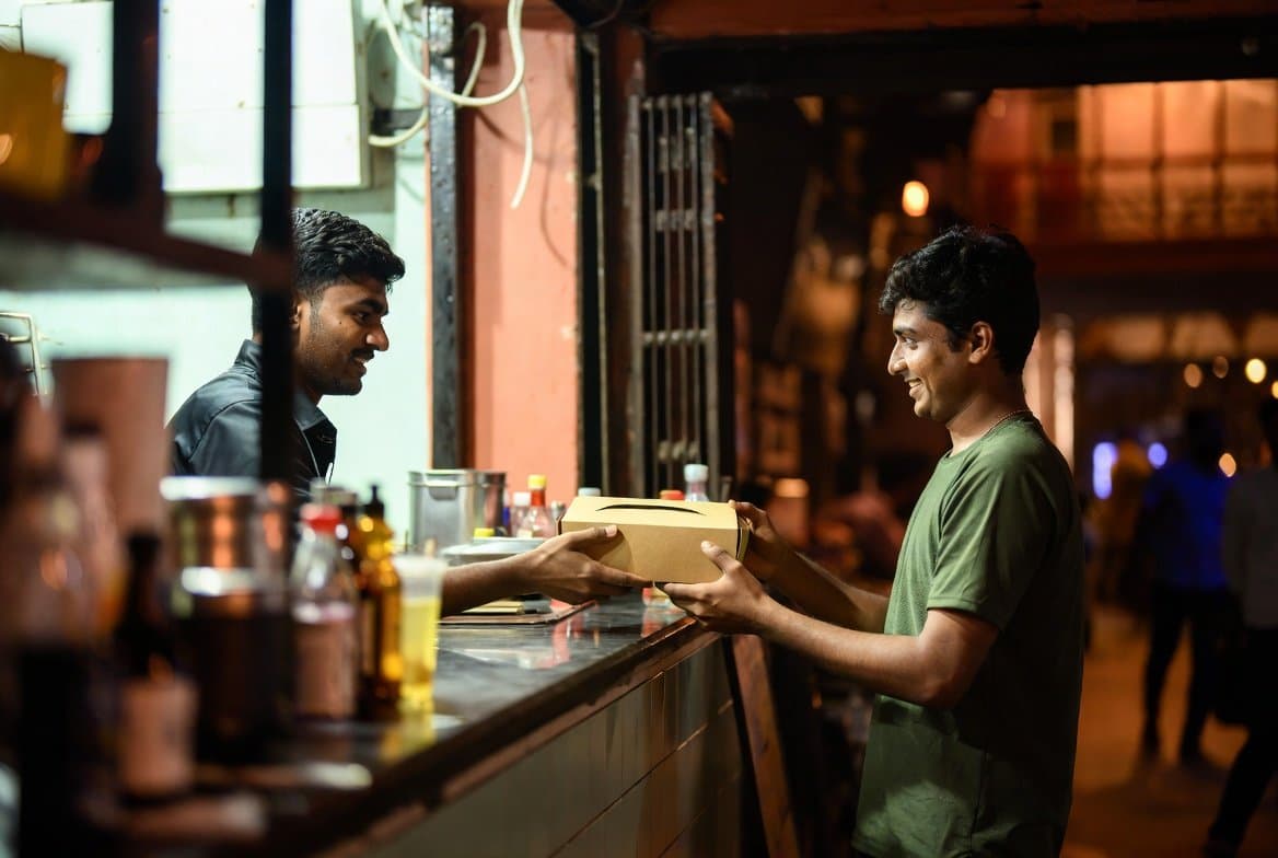 A restaurant staff member handing a packaged meal to a customer at the counter